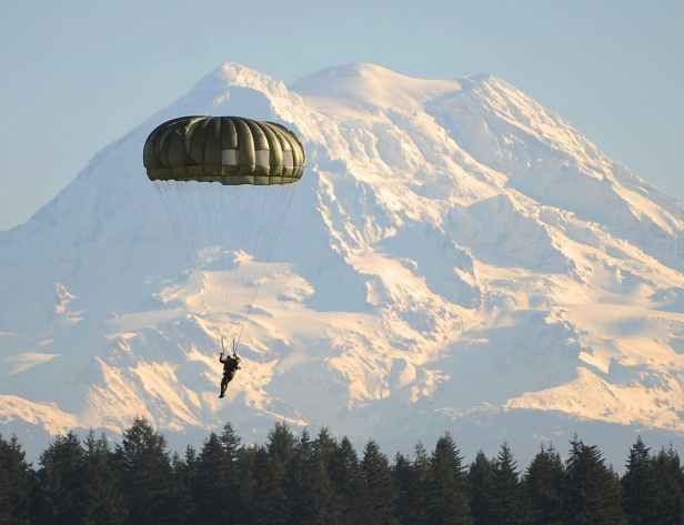 man flying on parachute near green trees